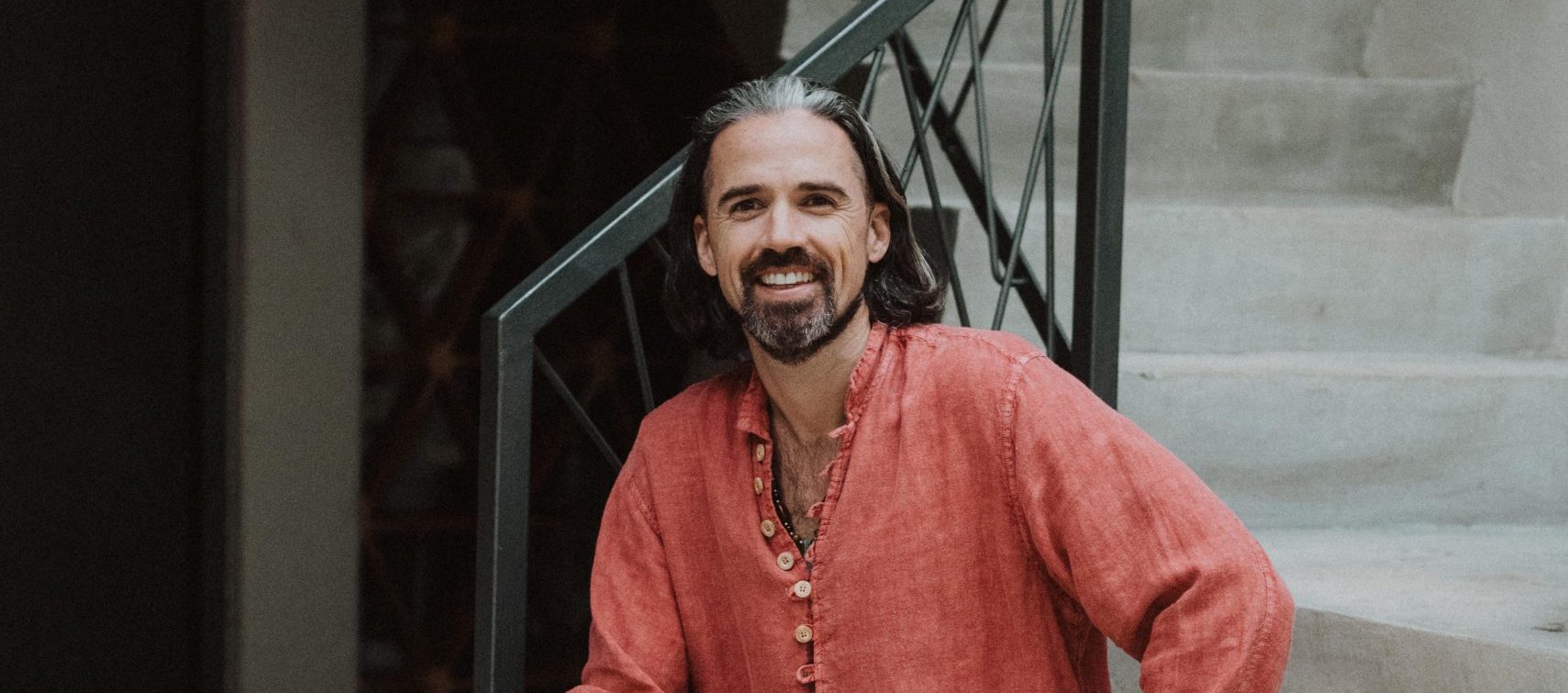 Smiling investor in red linen shirt seated on stairs—conscious capital and values-aligned